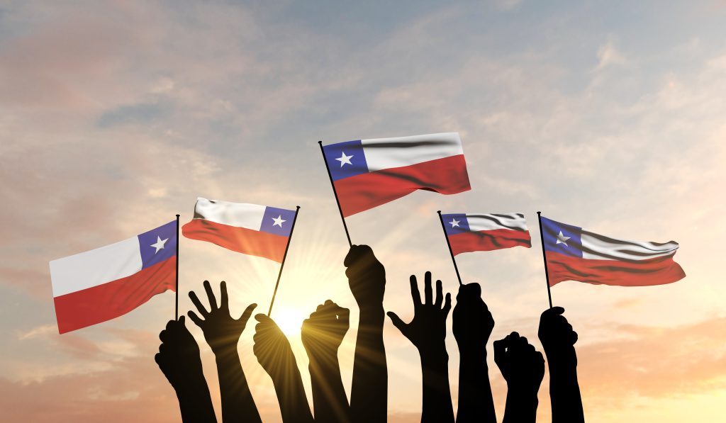 Personas levantando banderas de Chile al atardecer durante la celebración de Fiestas Patrias, simbolizando orgullo y unión nacional.